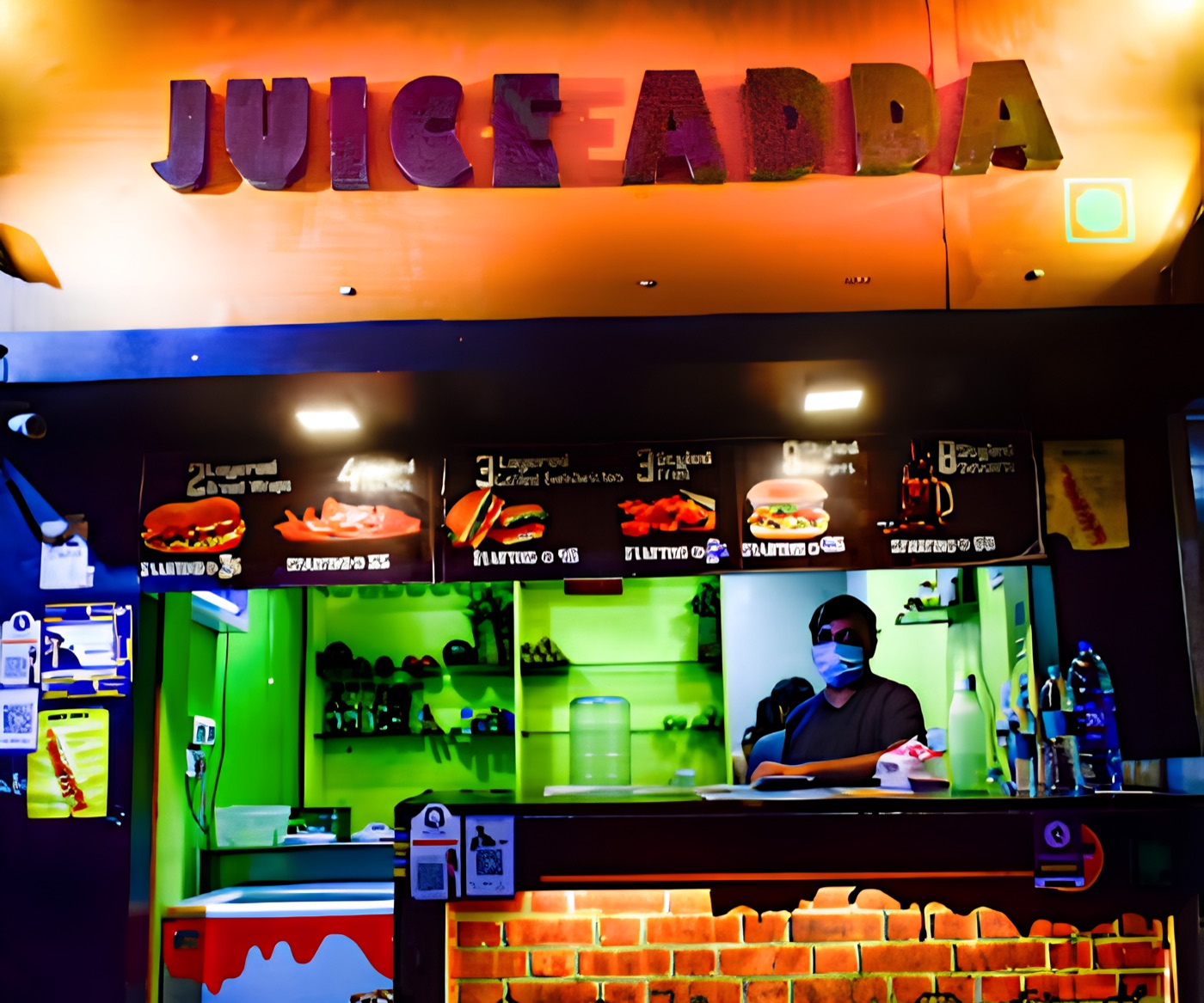The Juice Adda counter at night — the menu boards lit, someone at the till